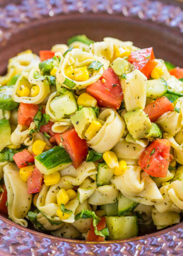 A colorful bowl of pasta salad with tomatoes, cucumbers, corn, and avocado.