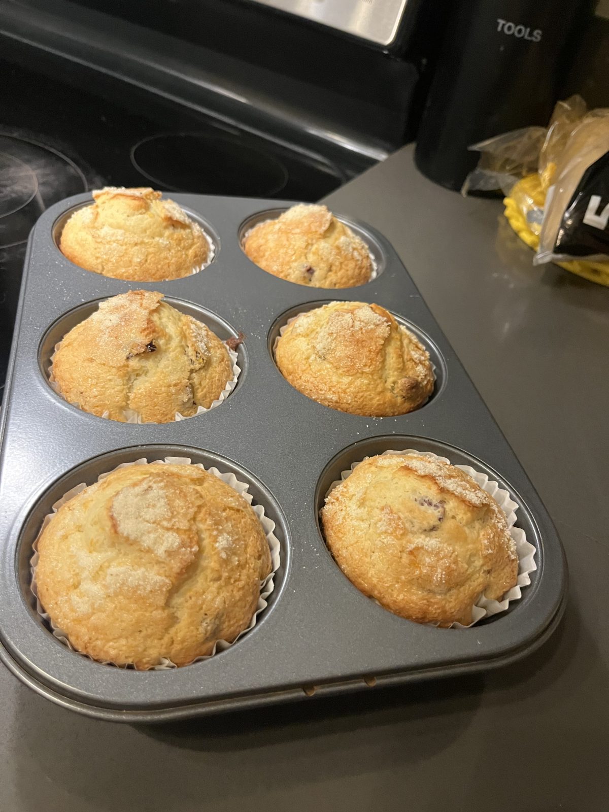 Six freshly baked muffins in a muffin tin on a kitchen counter.