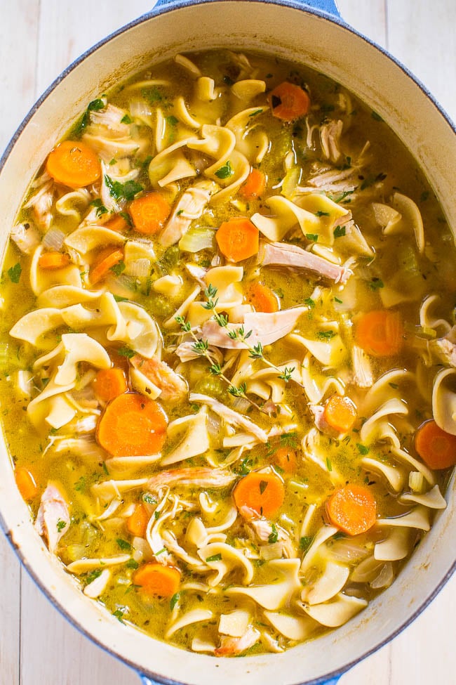 An overhead view of chicken noodle soup in a blue Dutch oven. 