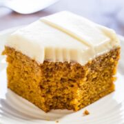 A slice of carrot cake with cream cheese frosting on a white plate.