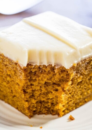 A slice of carrot cake with cream cheese frosting on a white plate.