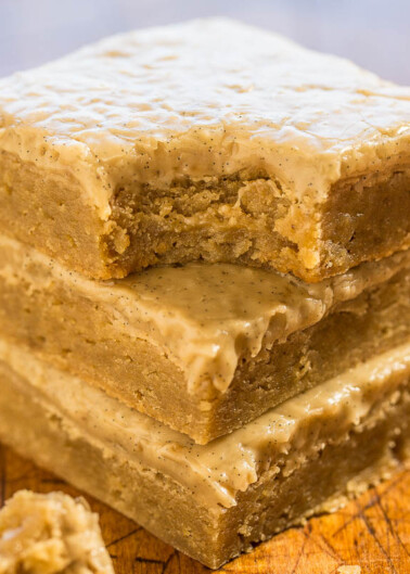 Stack of frosted blondies on a wooden surface.