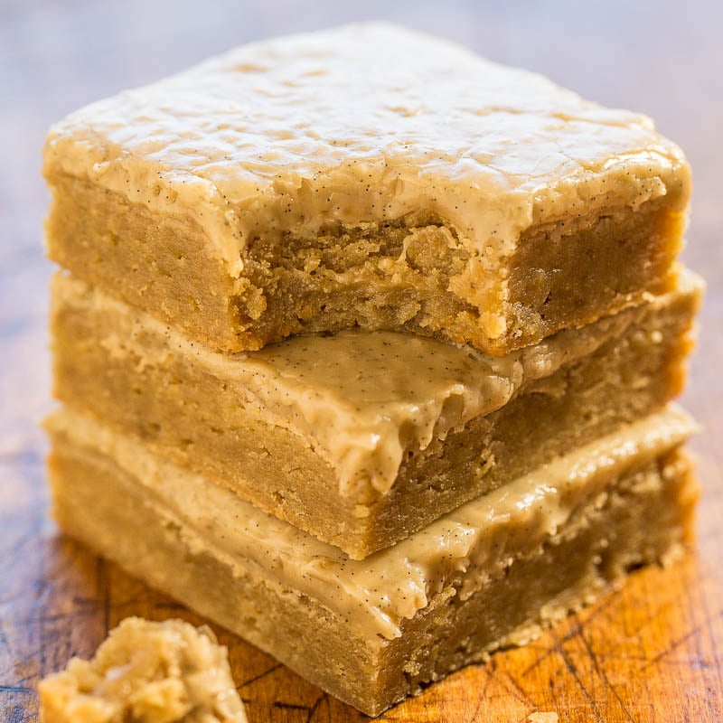Stack of frosted blondies on a wooden surface.