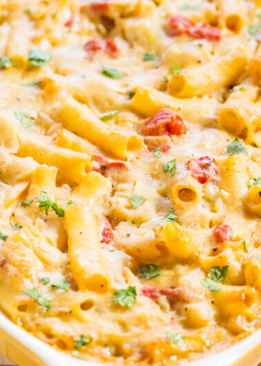 Baked cheesy pasta with tomato pieces and garnished with parsley in a baking dish.