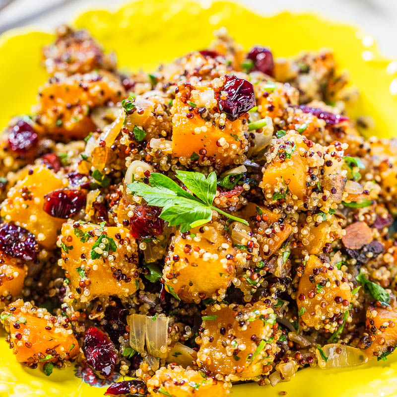 Quinoa salad with sweet potatoes, cranberries, and herbs served on a bright yellow plate.