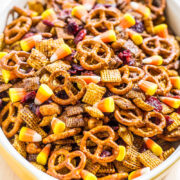 A bowl of snack mix containing pretzels, cereal, nuts, and dried fruits.