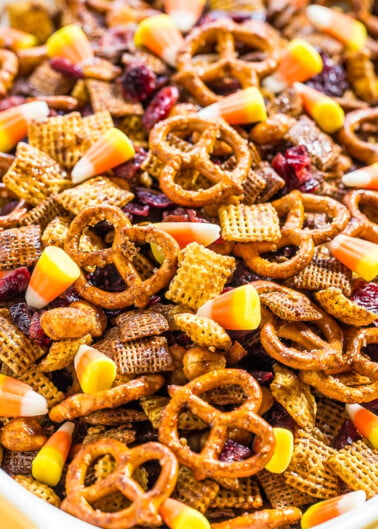 A bowl of snack mix containing pretzels, cereal, nuts, and dried fruits.