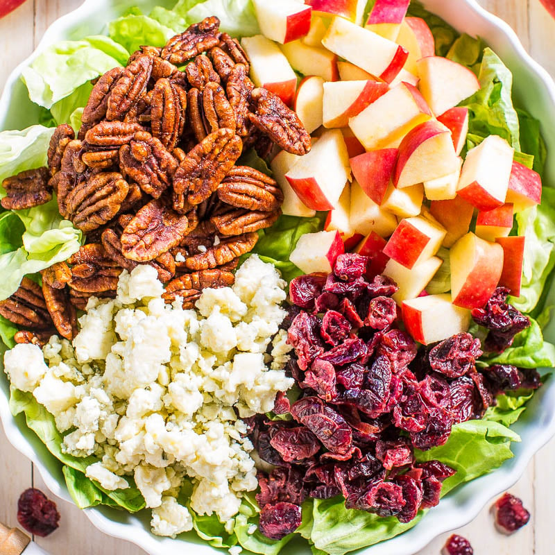 A fresh salad with green lettuce topped with apple pieces, candied pecans, dried cranberries, and crumbled cheese.