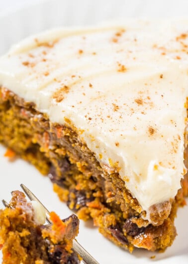 A slice of carrot cake with cream cheese frosting on a white plate, with a fork taking a bite out of it.