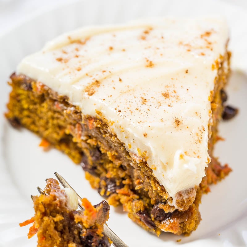 A slice of carrot cake with cream cheese frosting on a white plate, with a fork taking a bite out of it.