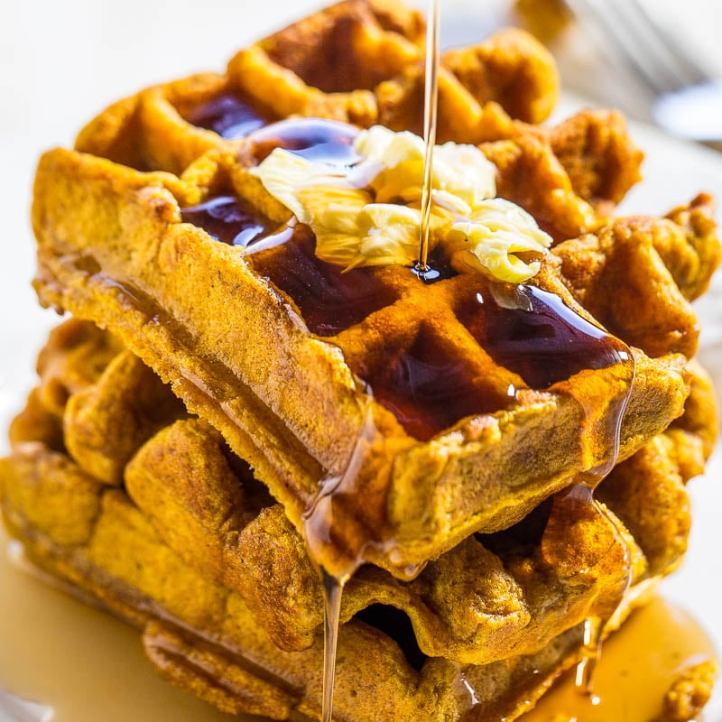Stack of waffles with butter and syrup being poured on top.