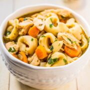 A bowl of chicken noodle soup with vegetables and herbs.