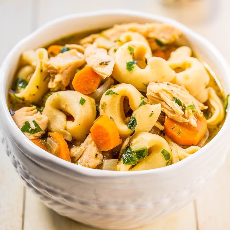 A bowl of chicken noodle soup with vegetables and herbs.