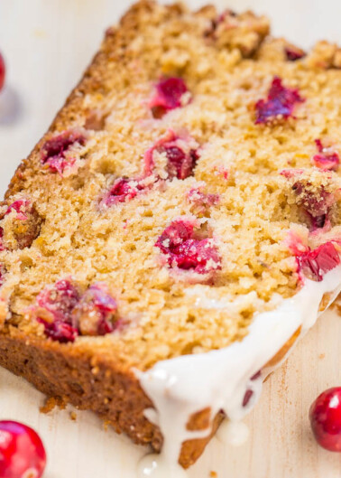 A slice of cranberry loaf cake with icing on a wooden surface.
