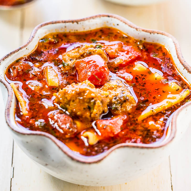 A bowl of stew with meatballs and vegetables in a rich, red sauce.