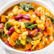 A bowl of colorful minestrone soup with pasta, beans, and vegetables.
