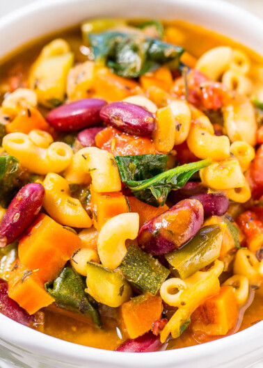 A bowl of colorful minestrone soup with pasta, beans, and vegetables.