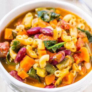 A bowl of vegetable minestrone soup with pasta, beans, and leafy greens.