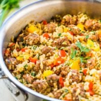 A skillet filled with a colorful rice dish mixed with ground meat, bell peppers, tomatoes, and garnished with fresh parsley.