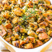 A baking dish filled with golden-brown cubed stuffing garnished with fresh rosemary.