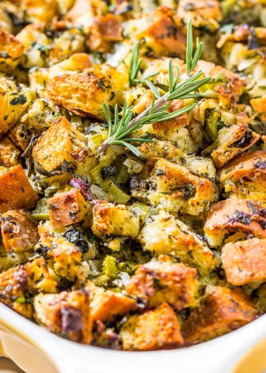 A baking dish filled with golden-brown cubed stuffing garnished with fresh rosemary.
