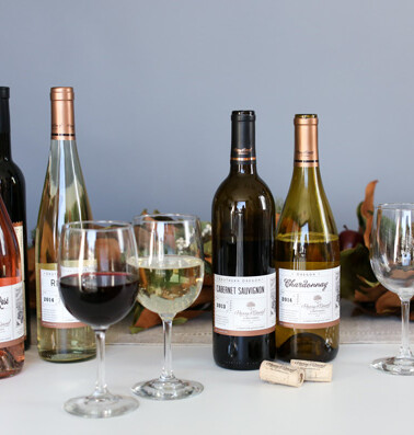 A selection of wine bottles and glasses on a table, with a bottle of red wine poured into one glass and white wine in another.