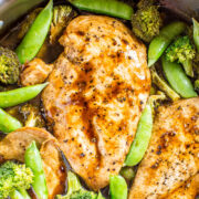 Grilled chicken breasts with broccoli and snap peas in a savory sauce.