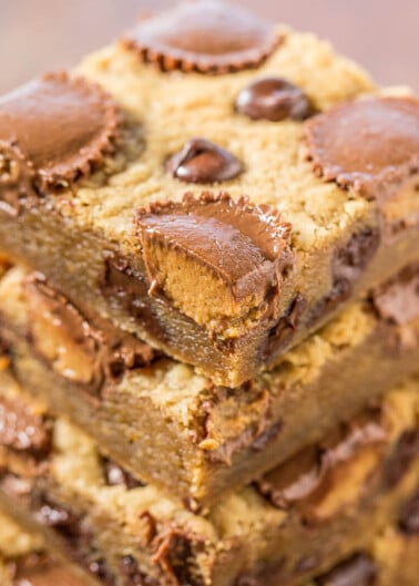 A stack of chocolate chip cookie bars with peanut butter cups on a wooden surface.