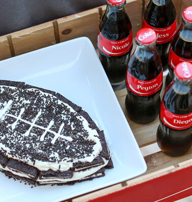 A plate of football-shaped dessert with custom-labeled coca-cola bottles displaying personal names.