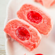 Sliced pieces of pink marzipan with a red candied cherry center on a white plate.