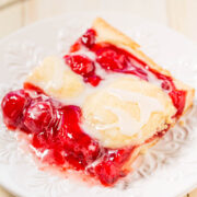 A slice of cherry pie topped with melting vanilla ice cream on a white plate.