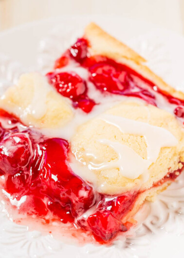 A slice of cherry pie topped with melting vanilla ice cream on a white plate.