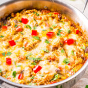 A skillet with a melted cheese-topped dish, garnished with diced tomatoes and fresh cilantro.