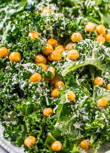A plate of kale salad topped with roasted chickpeas and grated cheese.
