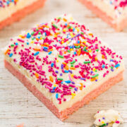 A piece of strawberry sheet cake with white frosting and colorful sprinkles.