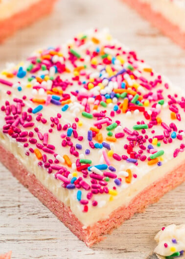 A piece of strawberry sheet cake with white frosting and colorful sprinkles.