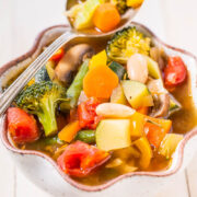A colorful bowl of vegetable soup with broccoli, carrots, tomatoes, and mushrooms.