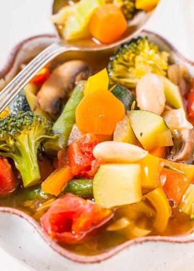 A colorful bowl of vegetable soup with broccoli, carrots, tomatoes, and mushrooms.