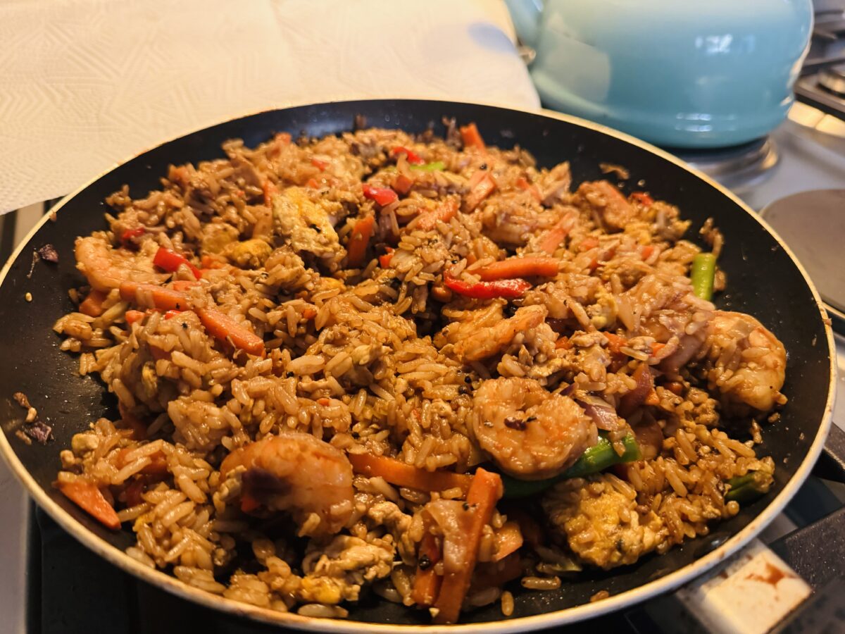A pan of fried rice with shrimp, vegetables, and scrambled eggs on a stovetop.