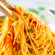 Chopsticks holding up a serving of stir-fried noodles with vegetables.