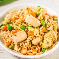 A bowl of chicken fried rice with vegetables and scrambled eggs.