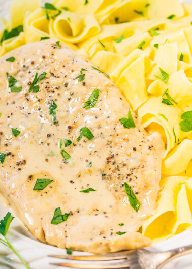Grilled chicken breast covered in a creamy sauce, served with ribbon pasta garnished with chopped parsley.