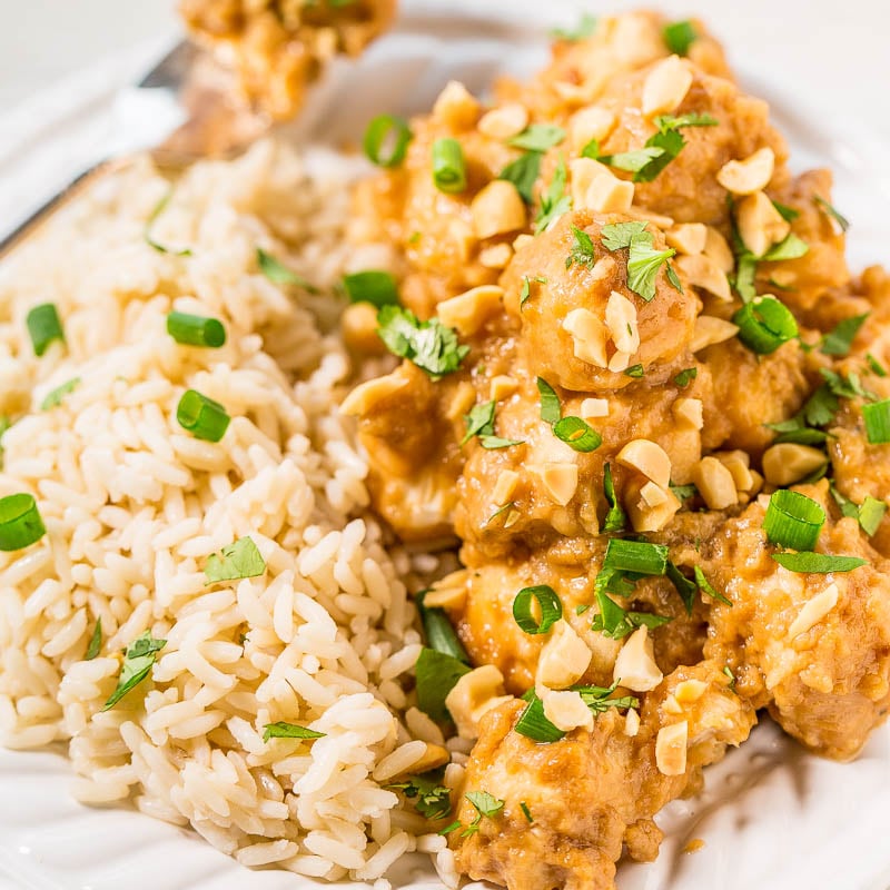 A plate of chicken with peanut sauce garnished with green onions, served alongside rice.