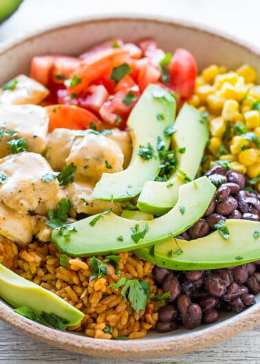 A bowl of rice with black beans, corn, avocado slices, tomatoes, and a creamy sauce.