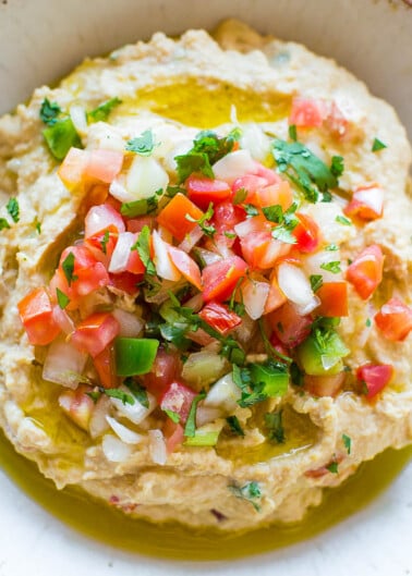 A bowl of hummus topped with fresh tomato salsa and a drizzle of olive oil.