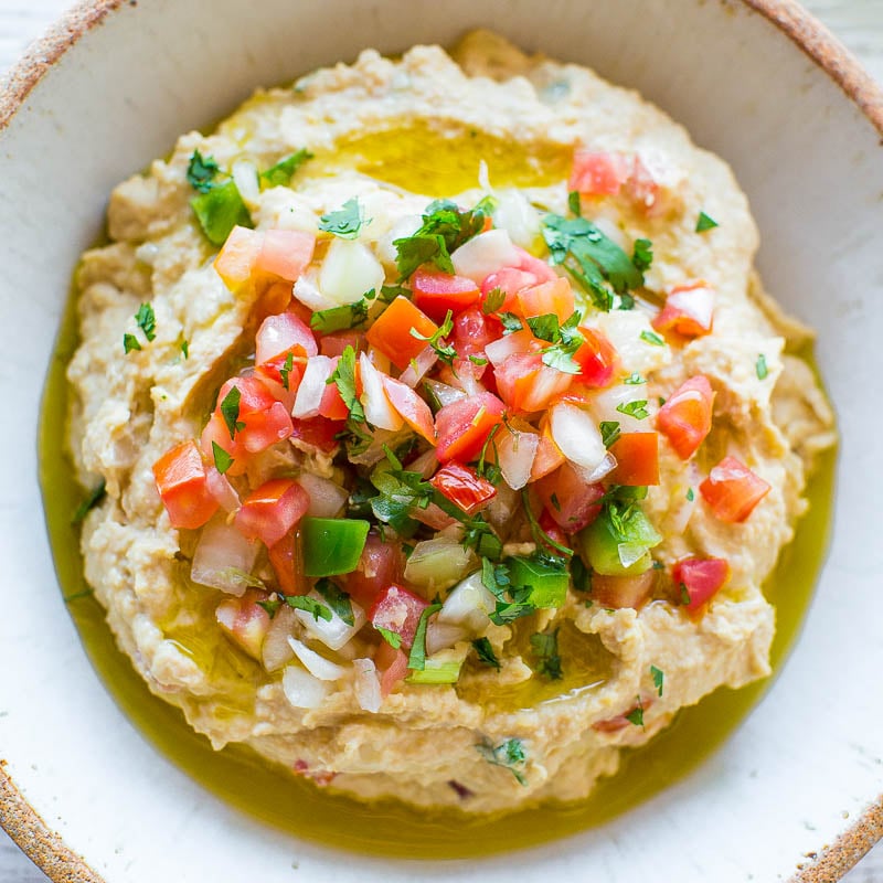 A bowl of hummus topped with fresh tomato salsa and a drizzle of olive oil.
