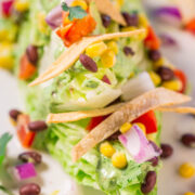 Close-up of a colorful avocado salad topped with tortilla chips, beans, and corn.