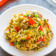 Scrambled eggs with sausage, bell peppers, and herbs on a white plate.