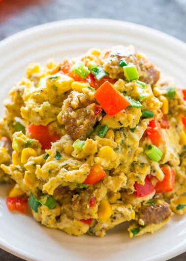 Scrambled eggs with sausage, bell peppers, and herbs on a white plate.