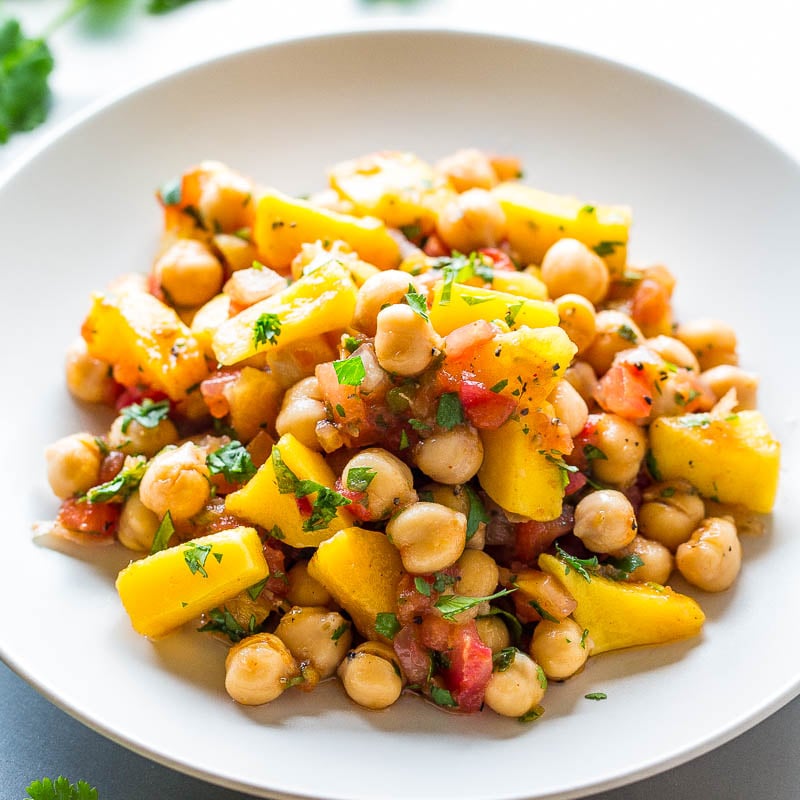 A plate of chickpea salad with mango, tomatoes, and fresh herbs.